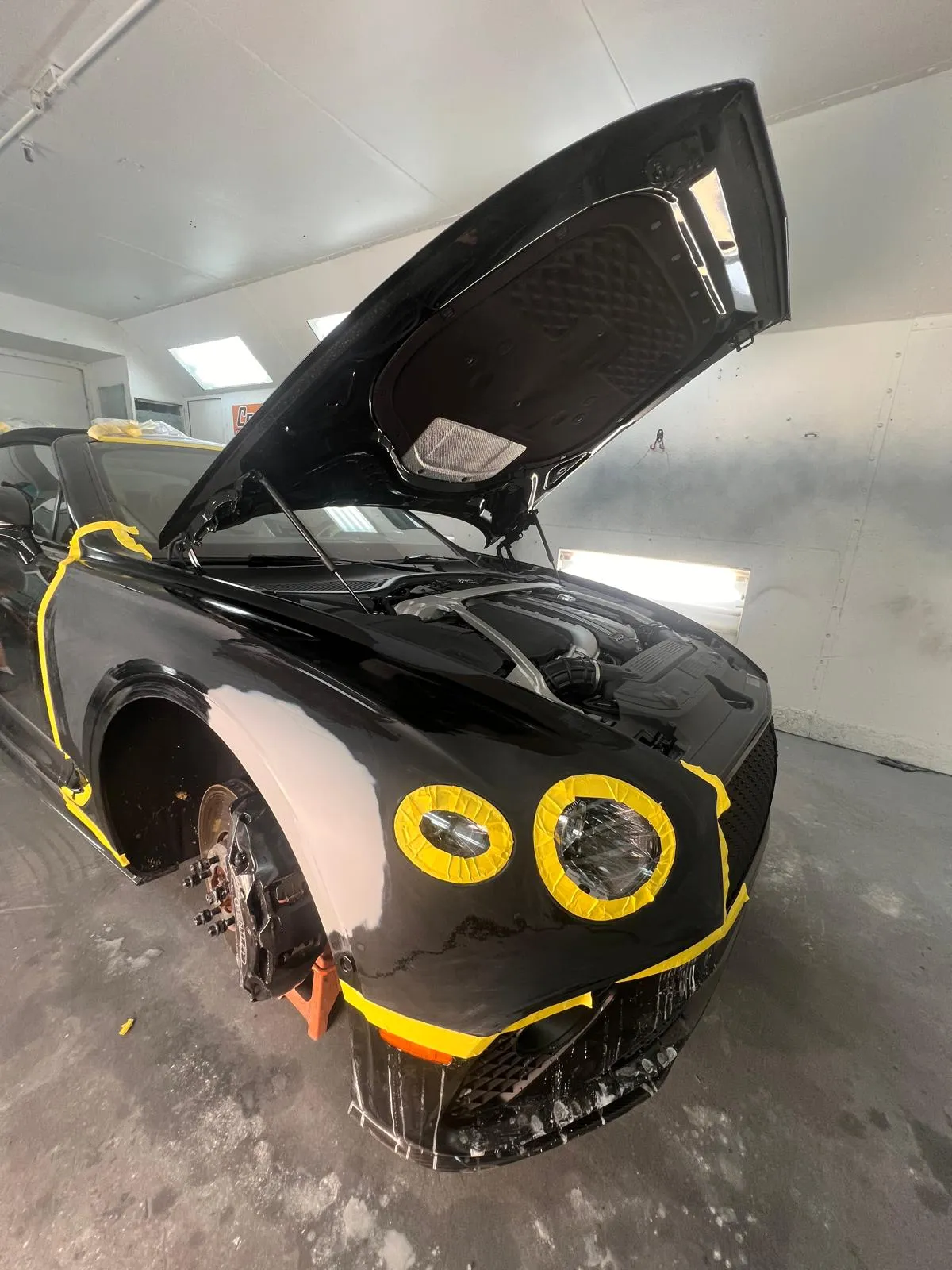 Black Bentley Continental GT masked with the hood open inside the paint booth