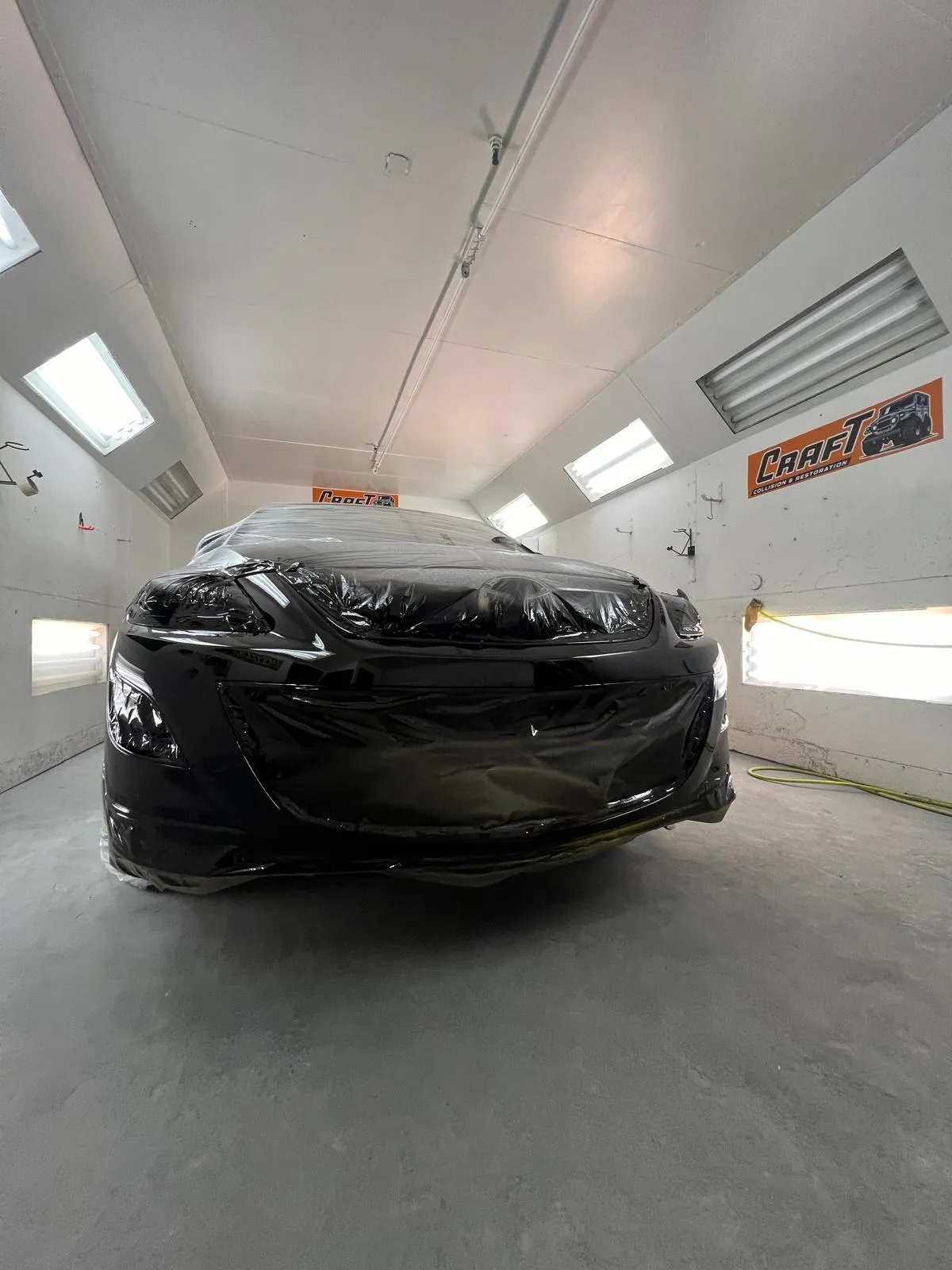 Black Mazda3 covered and masked inside the paint booth at Craft Collision