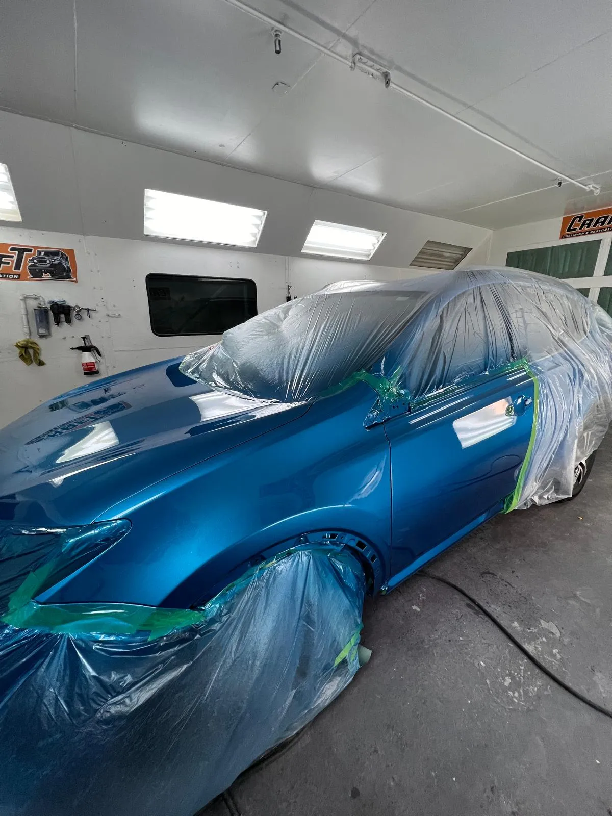 Blue Mazda masked and covered inside the downdraft paint booth