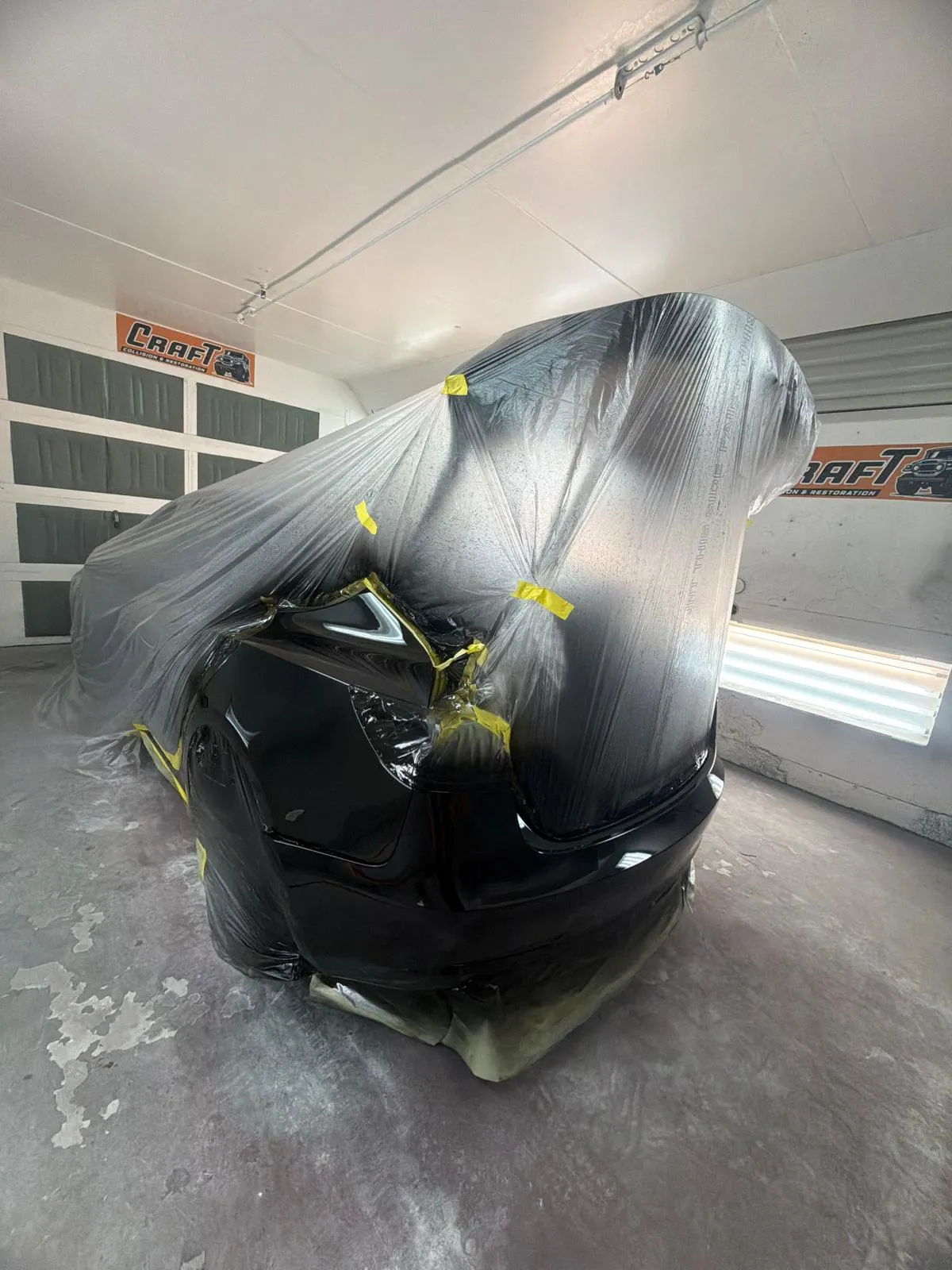 Black car wrapped in plastic with only the damaged bumper left exposed for a spot repair