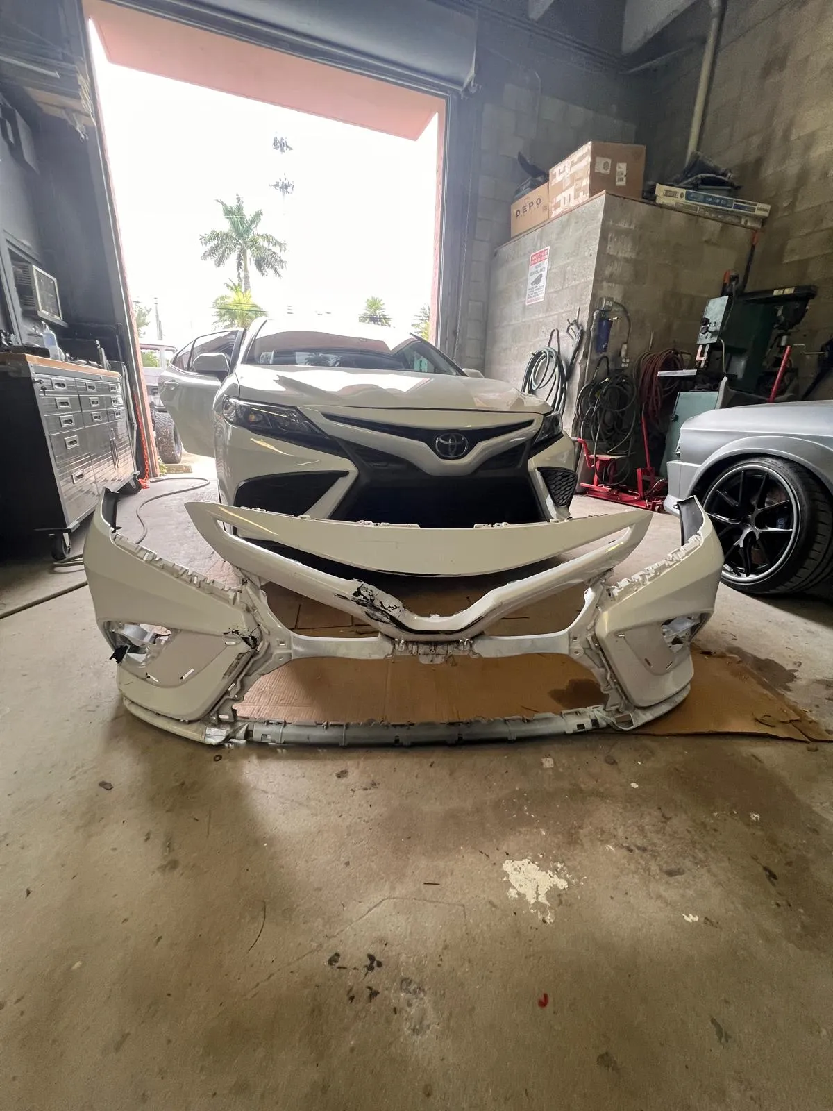 White Toyota Camry with the damaged front bumper cover removed before repair
