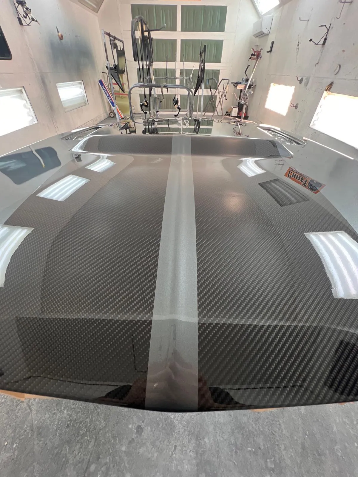 Carbon fiber hood with a center stripe under fresh clear coat inside the paint booth