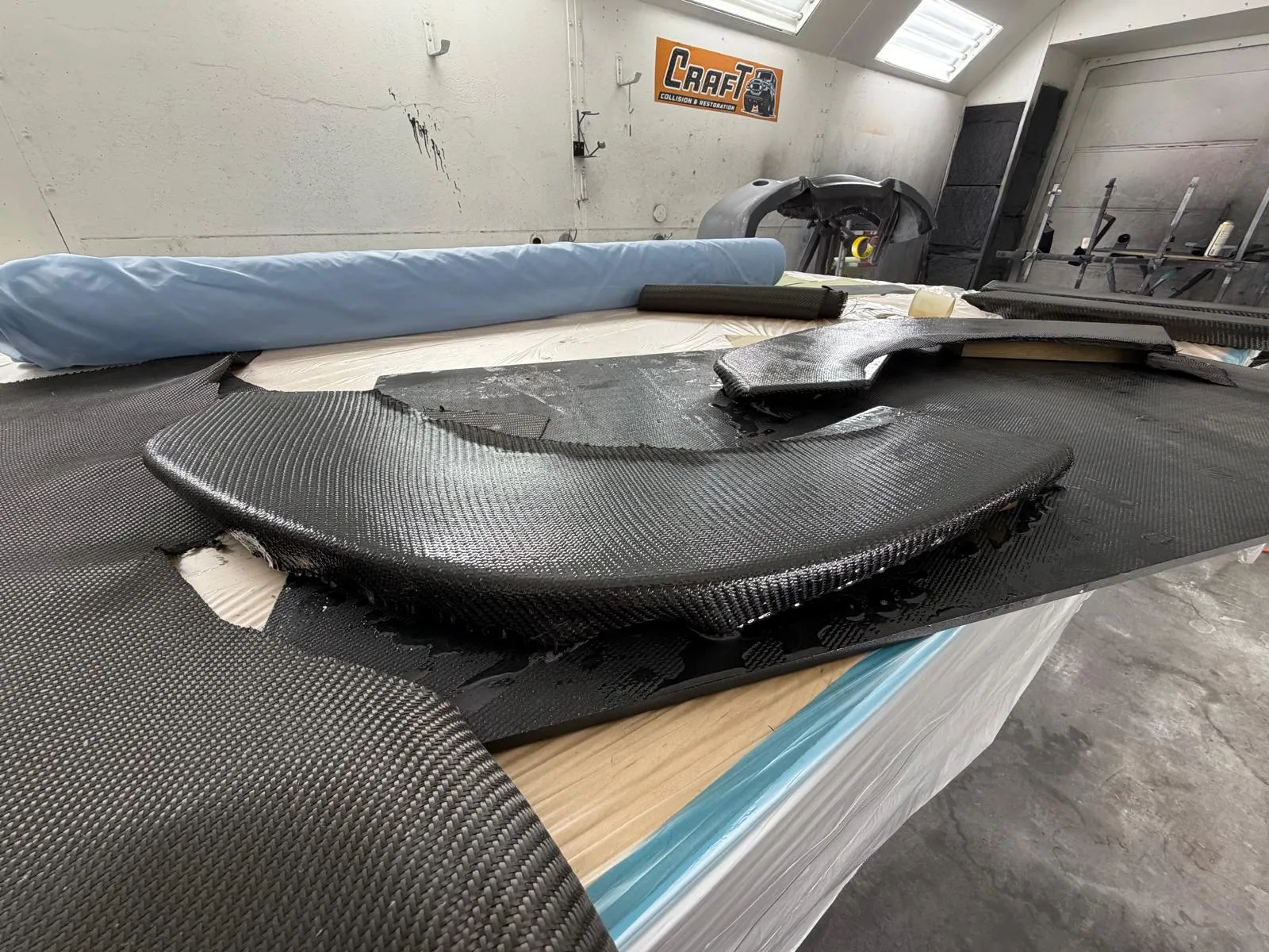 Carbon fiber part on the layup bench next to a roll of carbon fabric