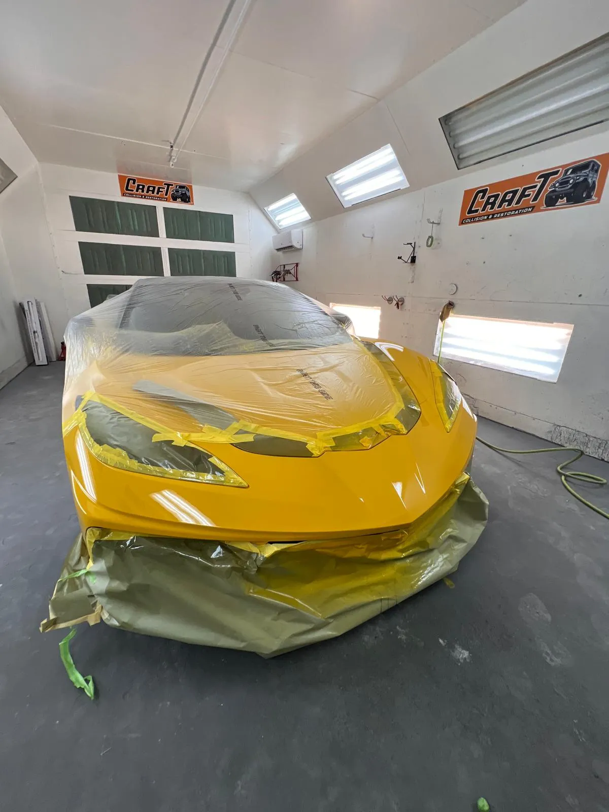 Yellow Corvette C8 masked with paper and tape inside the paint booth