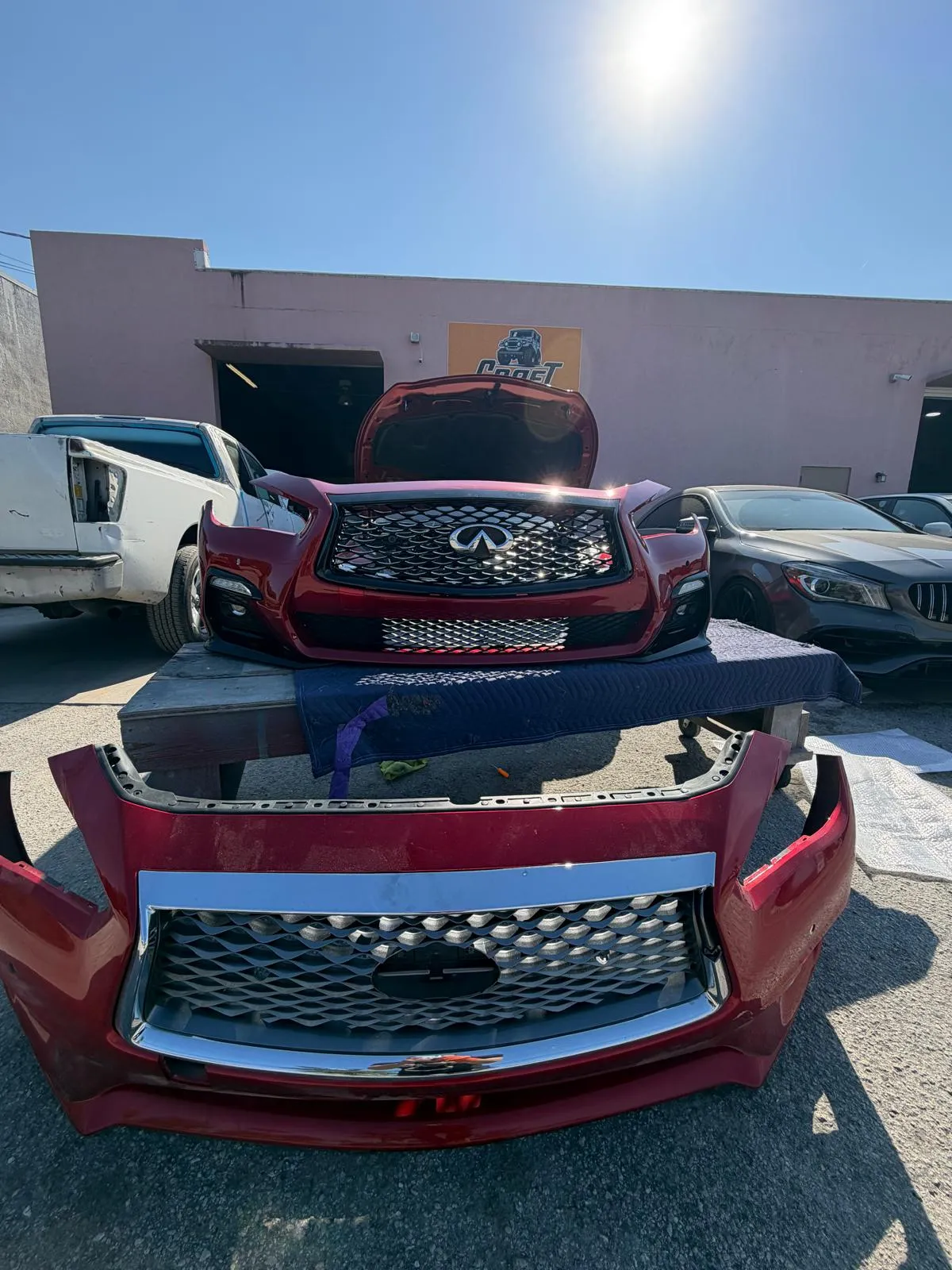 Red Infiniti front bumper cover and grille removed and laid out during collision repair