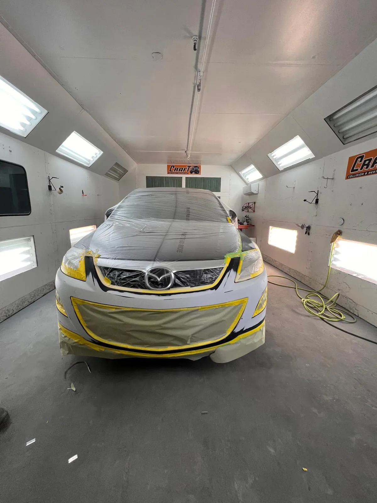 White Mazda with the front end masked in tape inside the spray booth