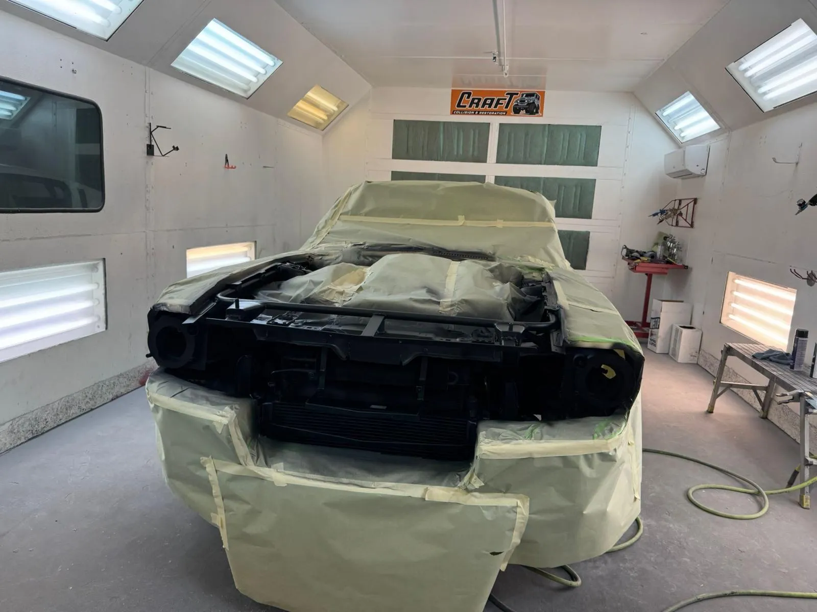 Mustang with the front bumper removed and the body masked inside the paint booth