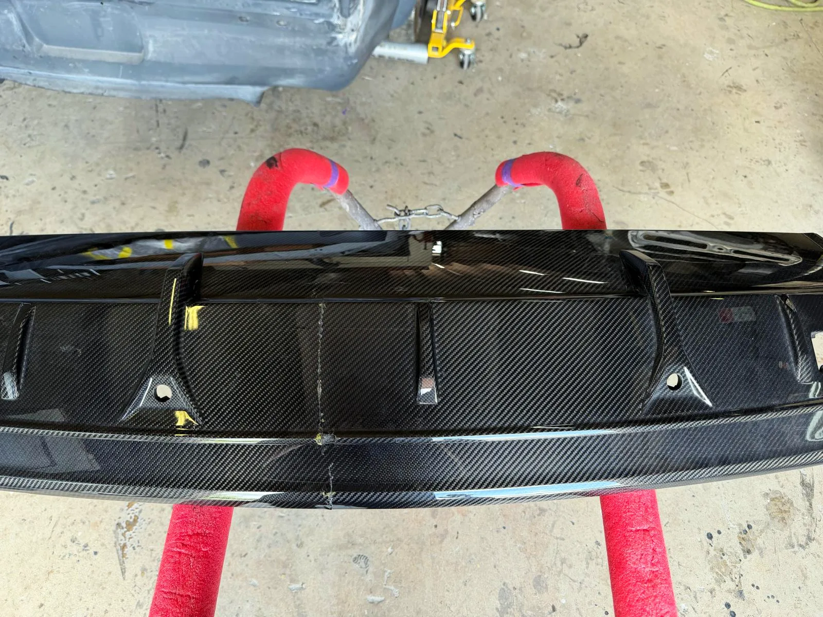 Damaged Lamborghini carbon fiber rear bumper on stands at Craft Collision, waiting to be repaired