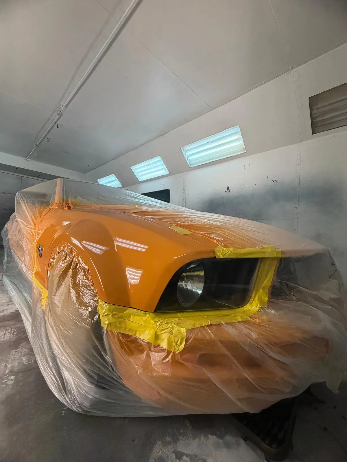 Orange Ford Mustang masked in the booth while the color is matched and blended