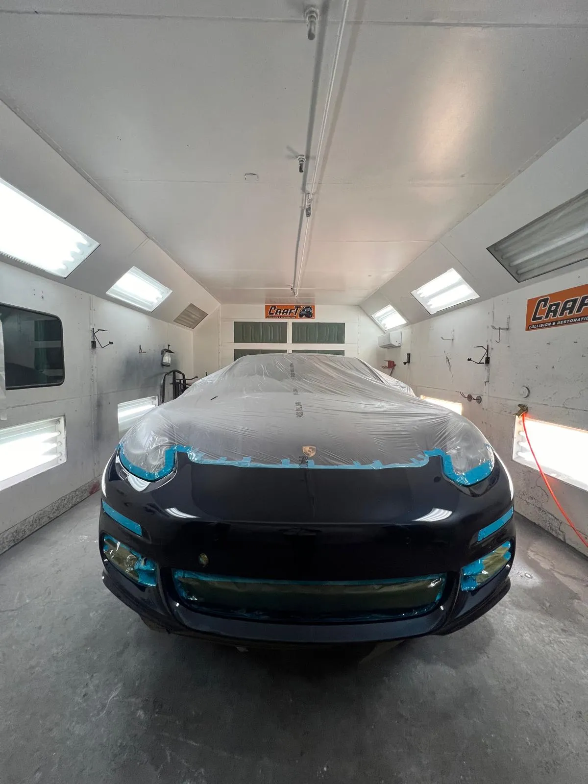Black Porsche Panamera with the front end masked inside the paint booth