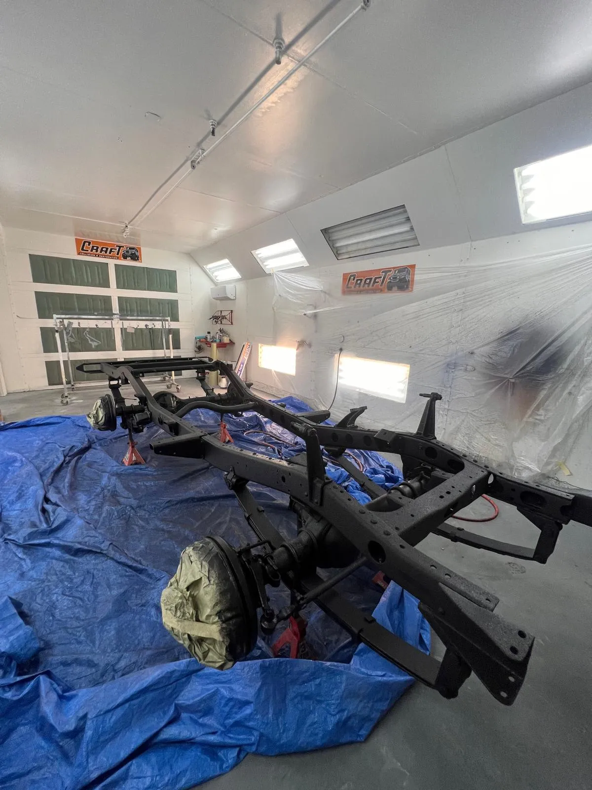 Bare truck chassis frame staged on a tarp inside the Craft Collision paint booth