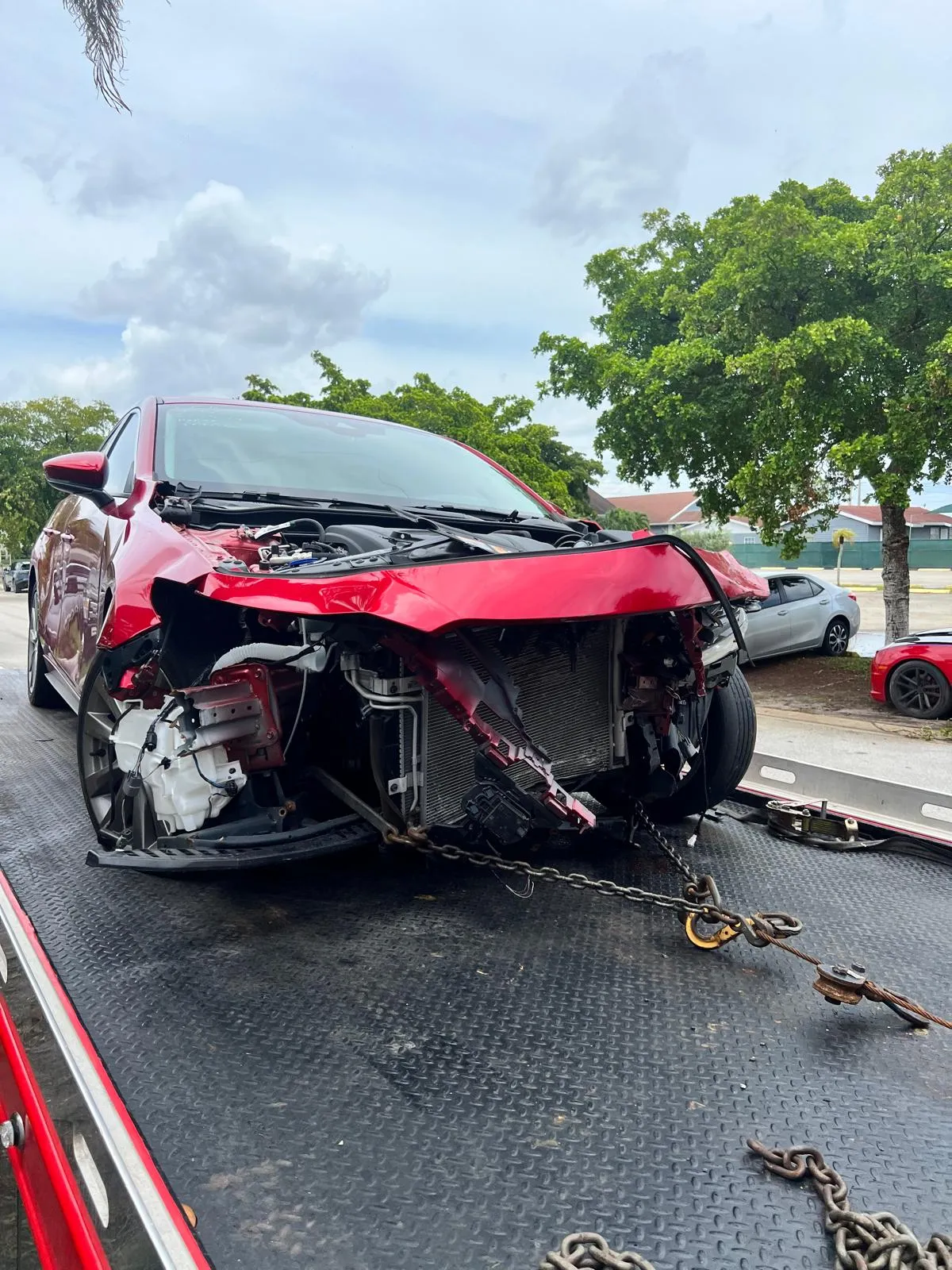 Red sedan with heavy front-end collision damage arriving on a flatbed tow truck